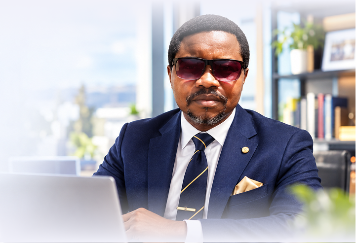 Emmanuel, a retired school principal in a navy suit, working on his laptop